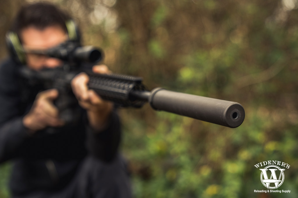 a photo of a man shooting a suppressed ar15 rifle outdoors