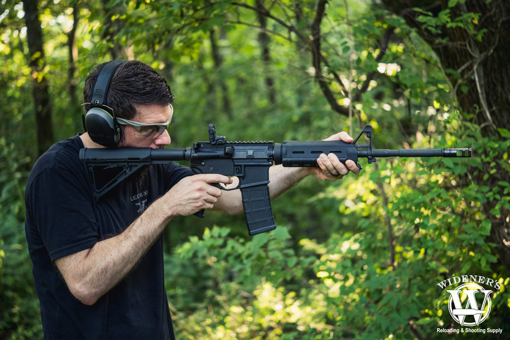 a photo of a man shooting an ar-15 rifle in the woods