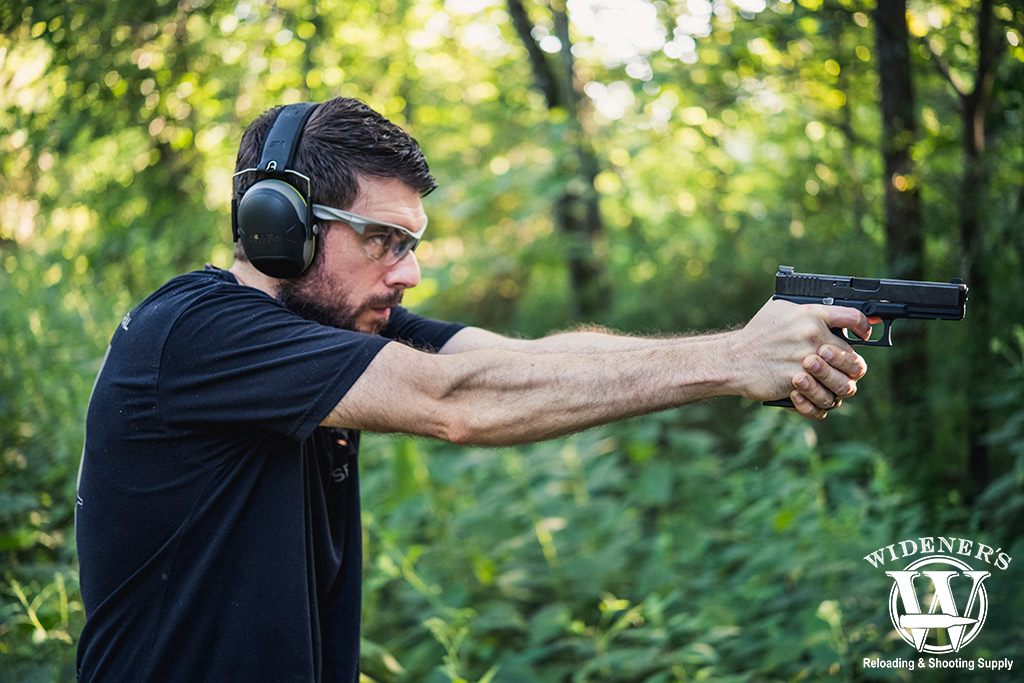 a photo of a man shooting a glock 17 pistol outdoors