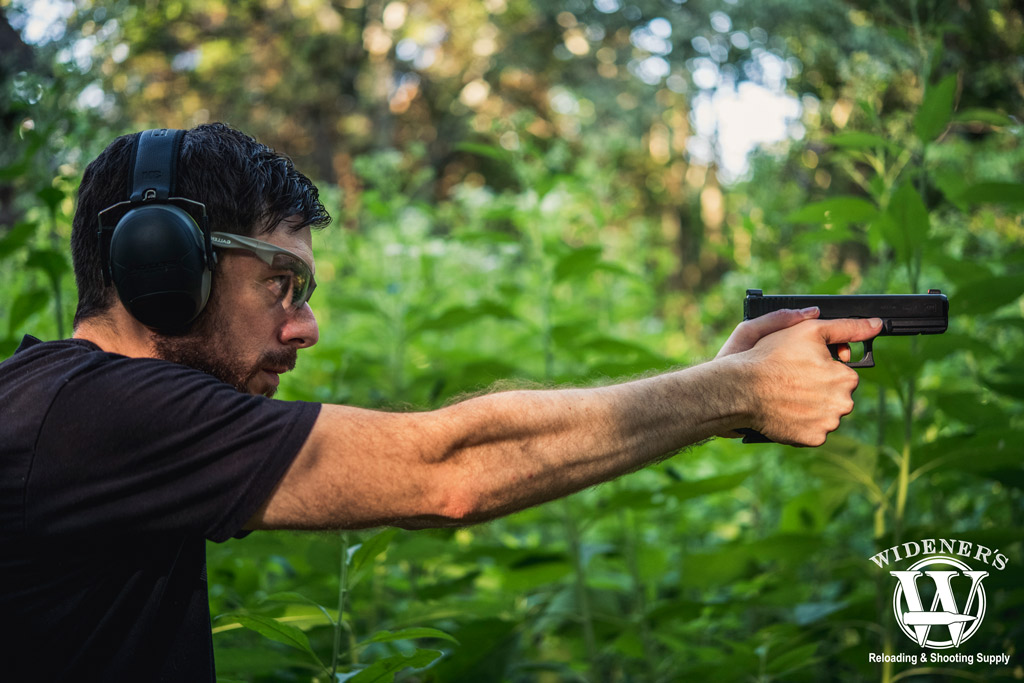 a photo of a man shooting a glock pistol outdoors