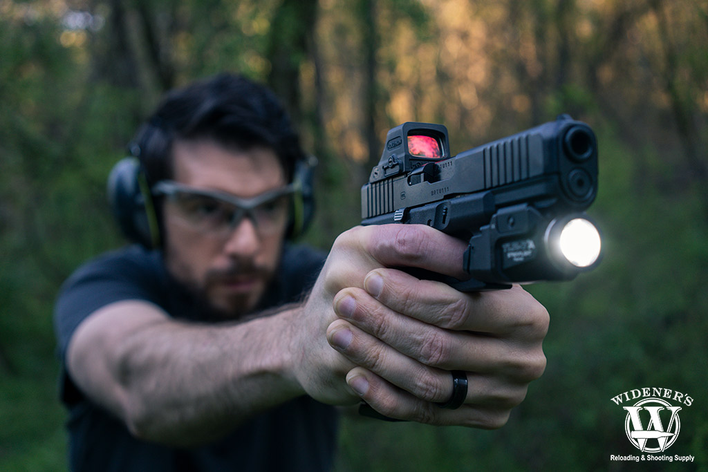 A photo of a man shooting a pistol outdoors red dot vs holographic