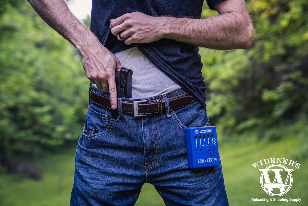 a photo of a male shooter using a shot timer at an outdoor gun range
