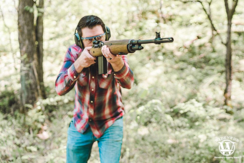 a photo of a man shooting a springfield m1a rifle in the woods