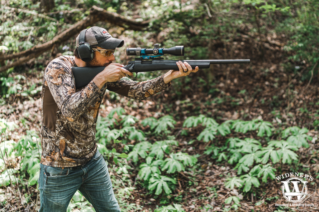a photo of a hunter shooting a rifle in the woods