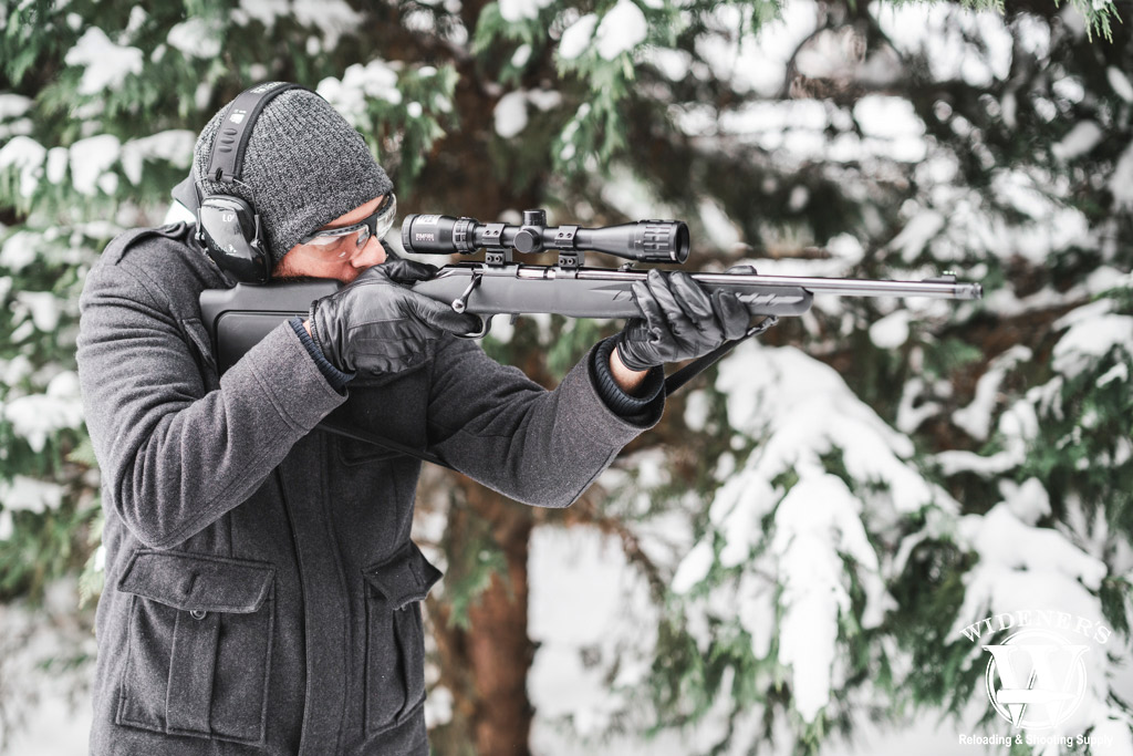 a photo of a man shooting a bolt action rifle in the snow