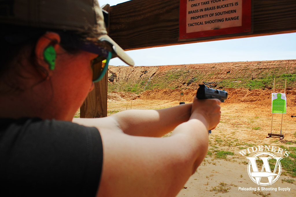 a photo of a female shooting a gun with iron sights at an outdoor range