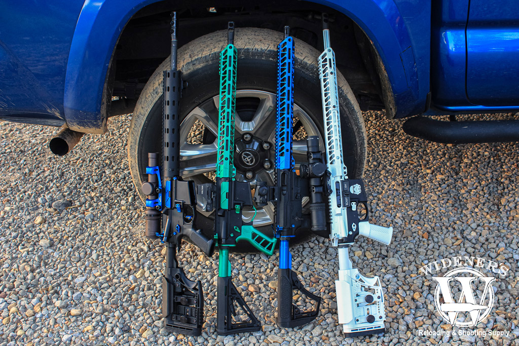 a photo of several custom AR-15 rifles leaning against a blue pickup truck