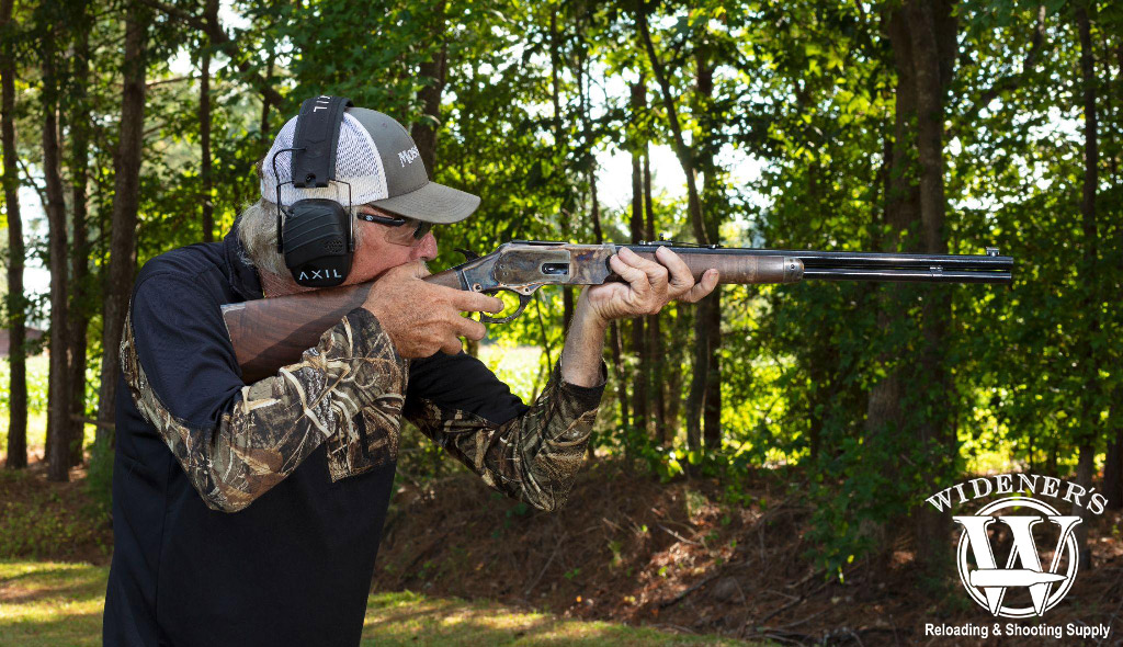 a photo of a man shooting a lever action rifle outdoors