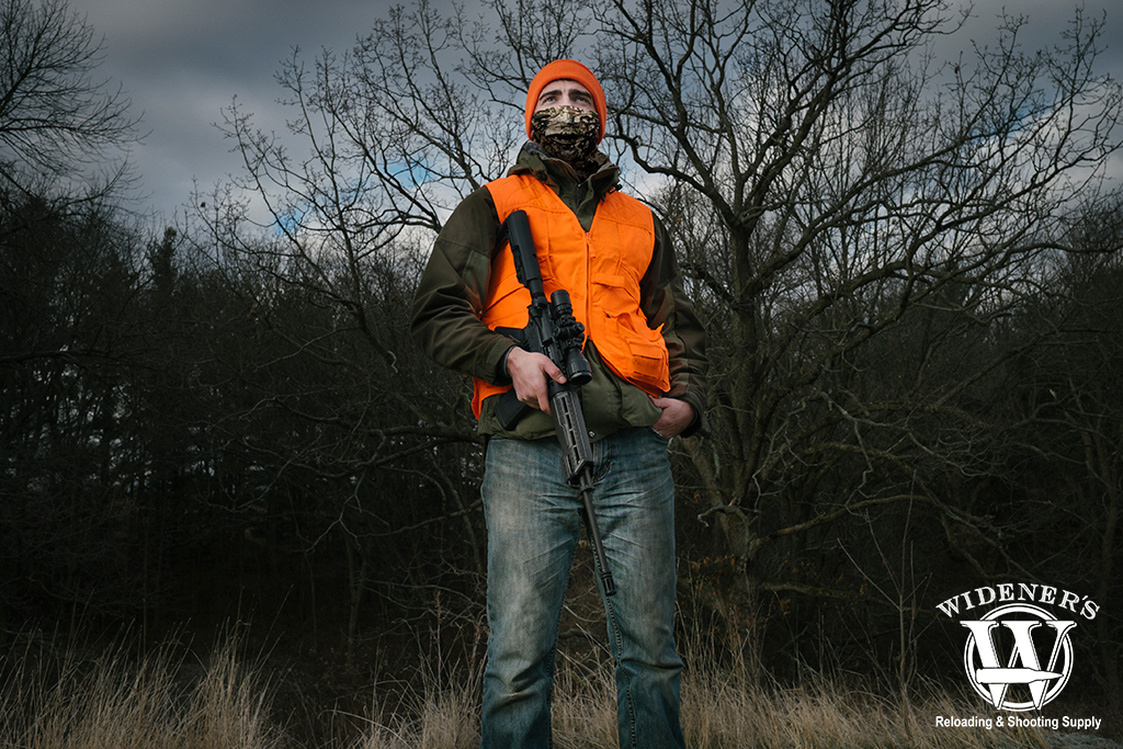 a photo of a man deer hunting in the woods with a rifle